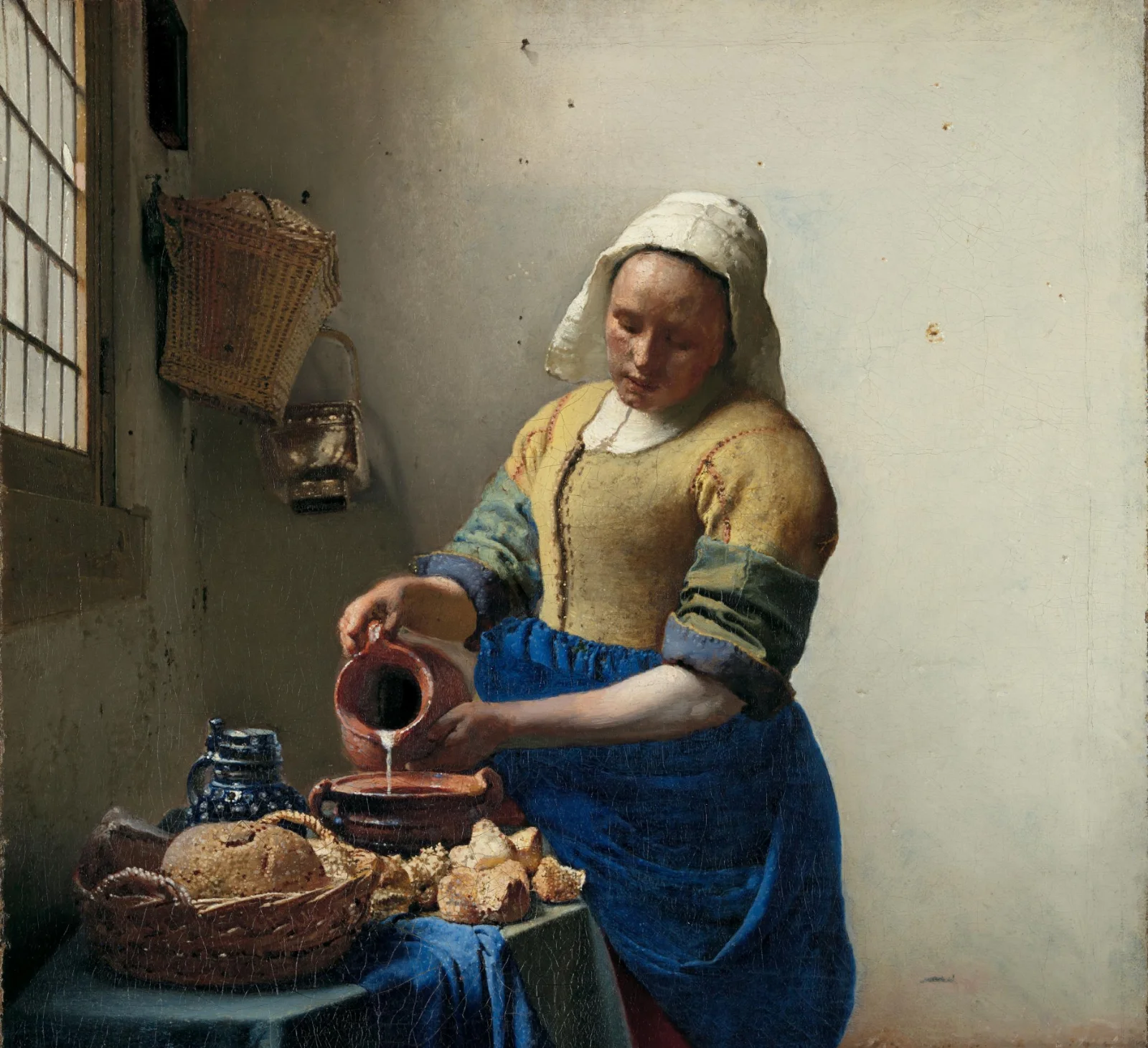 A woman pours milk beside a table of bread in a daylight-filled room